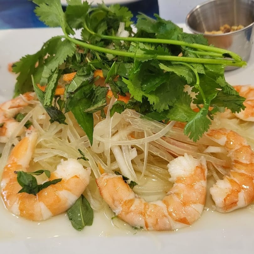 Vietnamese shrimp salad with shredded papaya, carrots, and fresh herbs on a white plate.
