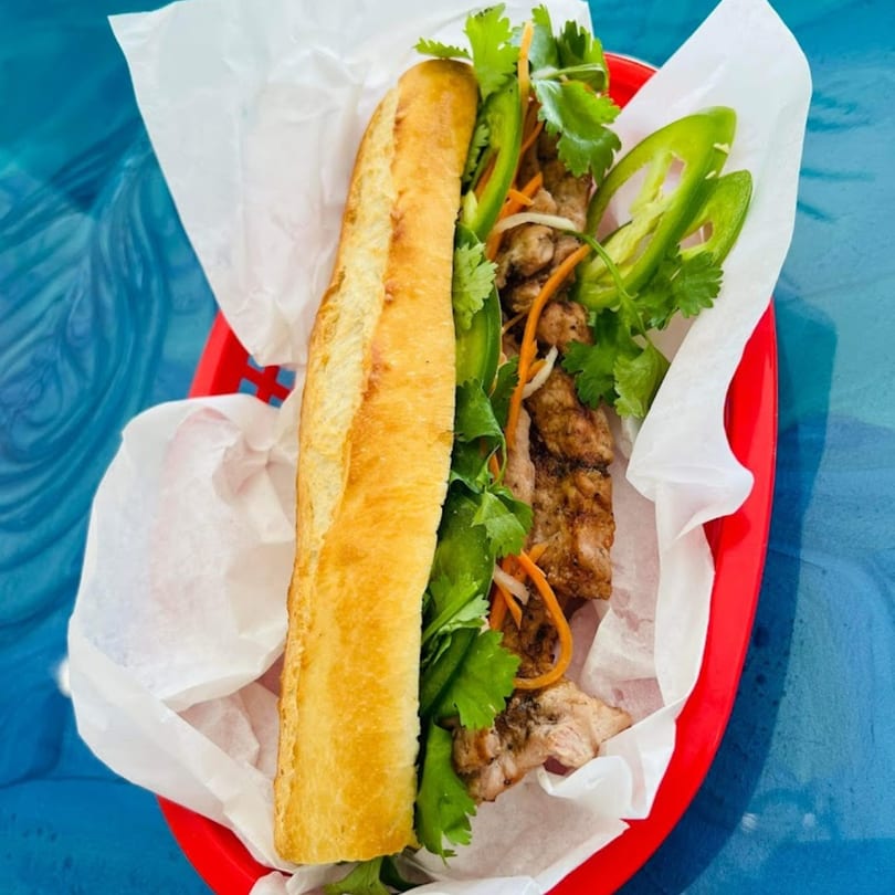 A Vietnamese banh mi sandwich with grilled meat, cilantro, and jalapeños in a red basket.
