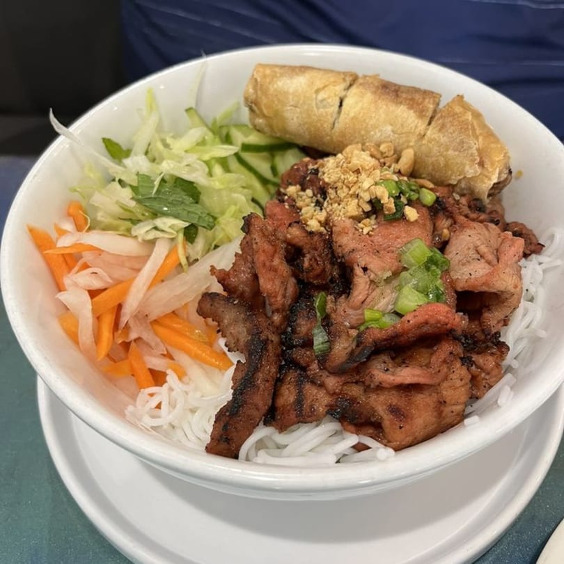 A Vietnamese vermicelli bowl with grilled pork, spring roll, pickled vegetables, and fresh herbs.