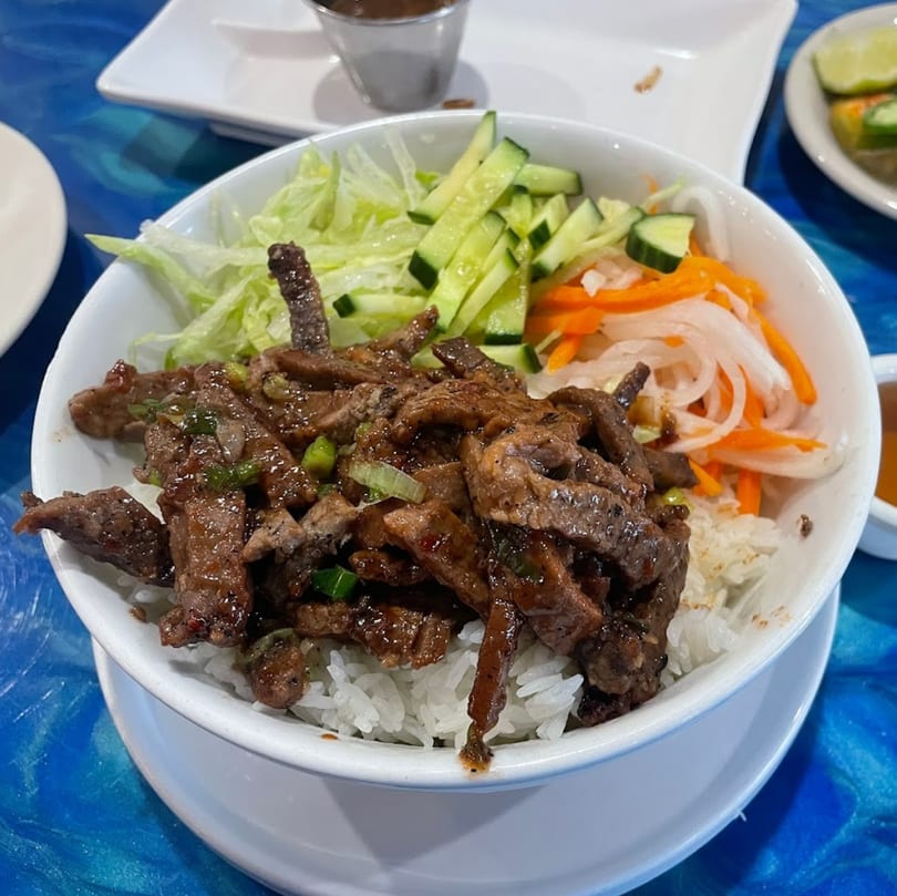A Vietnamese beef rice bowl with lettuce, cucumbers, and pickled carrots and daikon.
