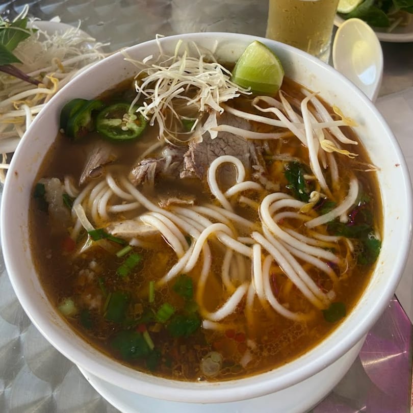 A bowl of Cafe LaVie Vietnamese pho with noodles, meat, bean sprouts, lime, and jalapeños.