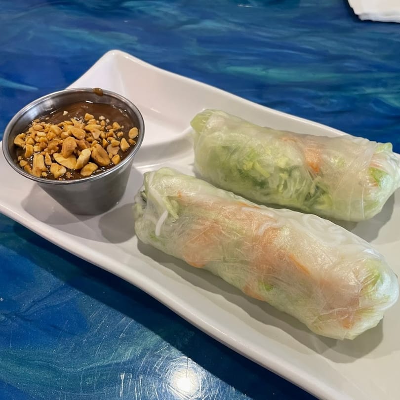 Two fresh Vietnamese spring rolls with peanut dipping sauce, topped with crushed peanuts, on a white plate.